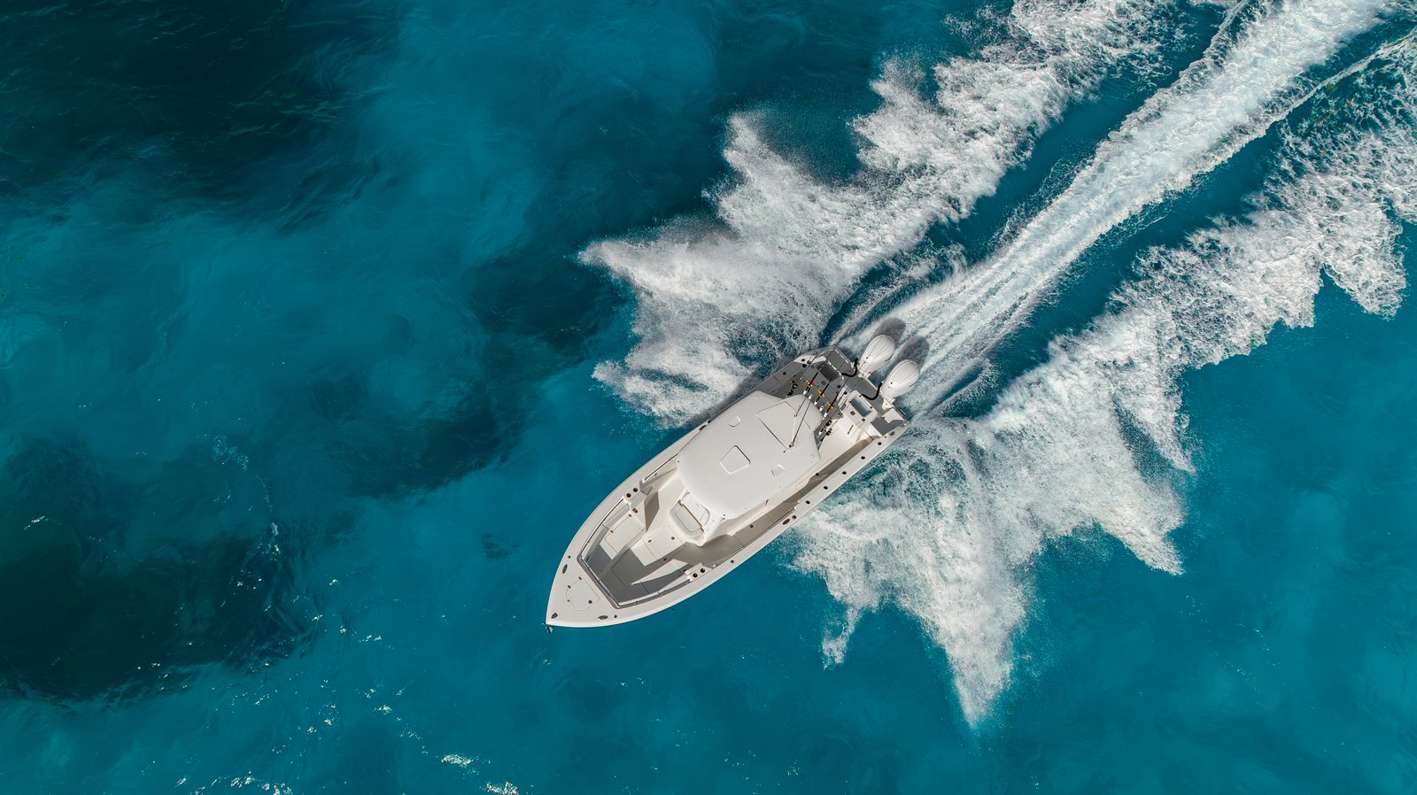 Overhead drone bow-first shot of Cobia 320 CC running over brilliant blue offshore water with wake