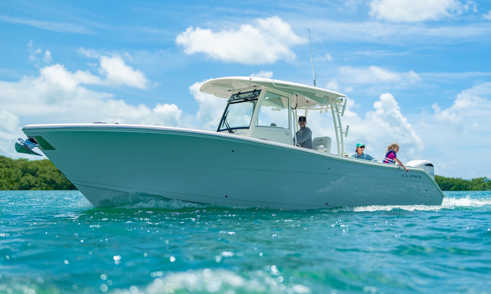 Water-level port side profile of Cobia 320 CC with family running near Florida coast, Cobia branding visible