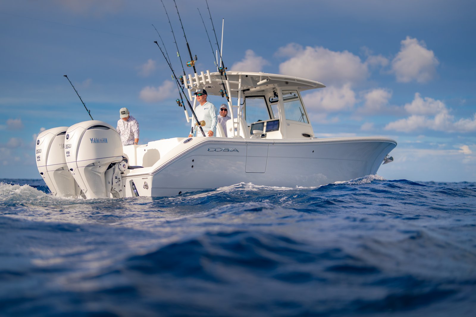 Cobia 320 CC port-stern running shot with three anglers fishing rods deployed over deep blue offshore water