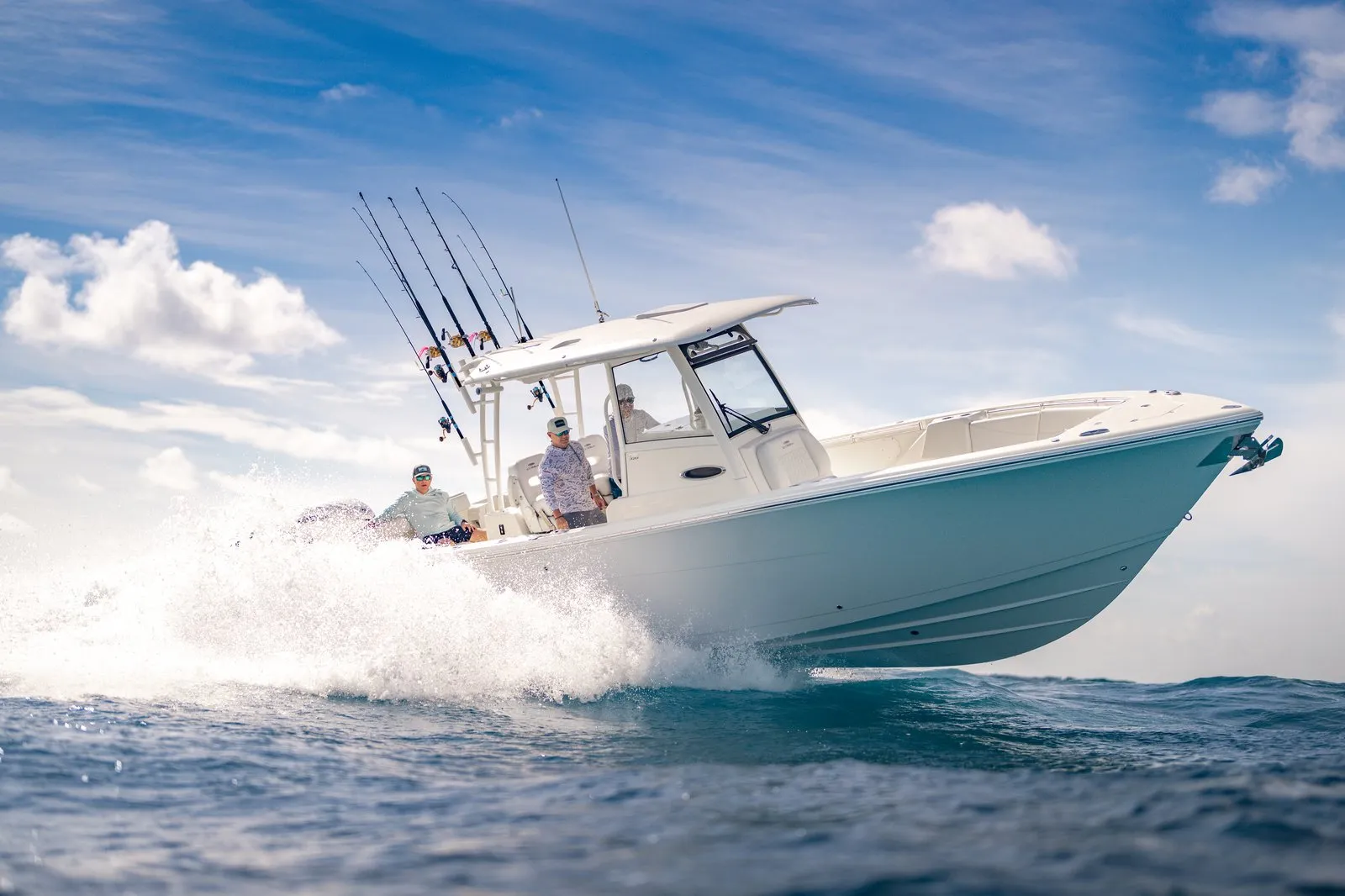 Bow-facing running shot of Cobia 320 CC with three anglers, Cobia hull branding, spray over blue water