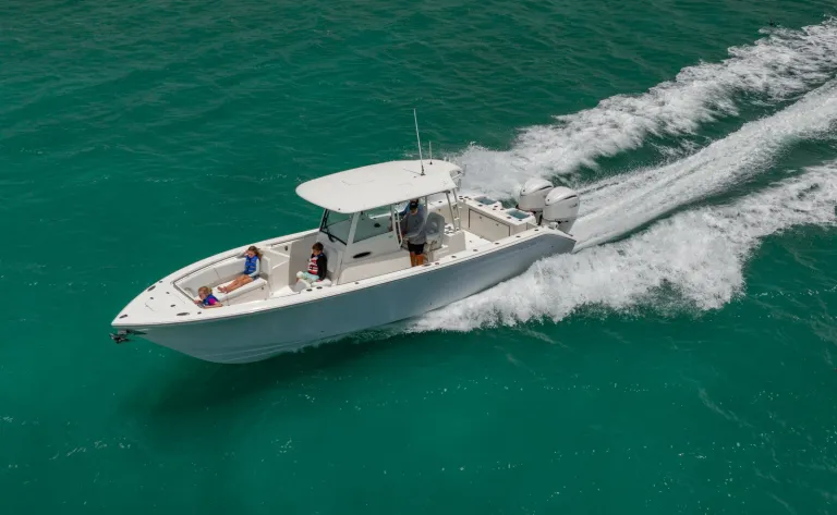 Aerial port-side drone shot of Cobia 320 CC with family on board running over turquoise green water