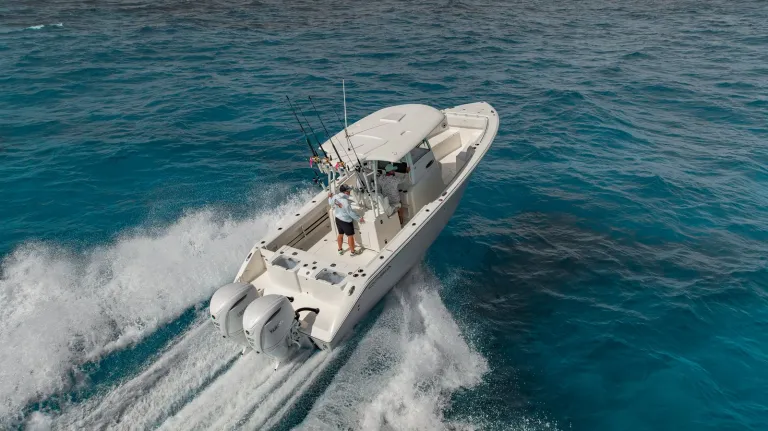 Aerial stern-quarter drone shot of Cobia 320 CC with angler at helm running over turquoise water