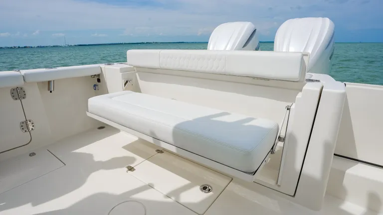 Cobia 320 CC aft cockpit seating area with white cushioned bench seat and fold-down bolster, blue ocean in background