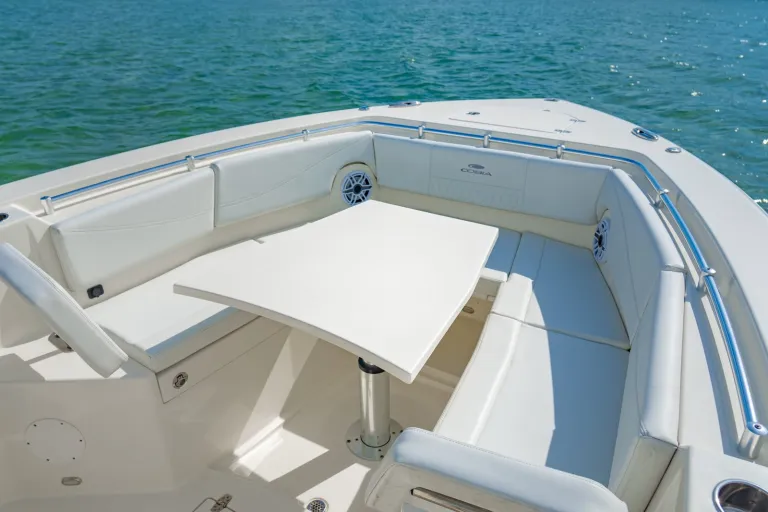 Cobia 320 CC bow lounge with electric pedestal dining table deployed, white cushioned U-seating, Cobia branding, and JL Audio speakers