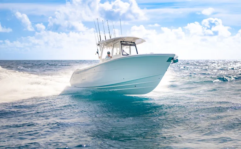 Bow-facing running shot of Cobia 320 CC cutting through waves over bright turquoise blue water