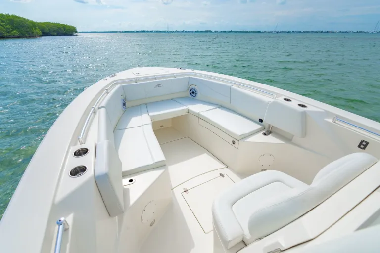 Cobia 320 CC bow U-shaped lounge seating with white cushions, JL Audio speaker, stainless steel bow rail, and clear turquoise water