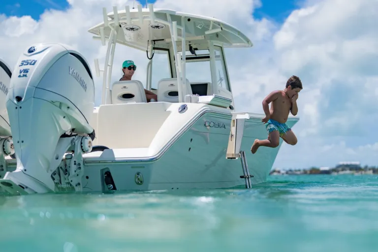 Boy jumping off stern boarding ladder of Cobia 320 CC with Yamaha 350 twin outboards into turquoise water