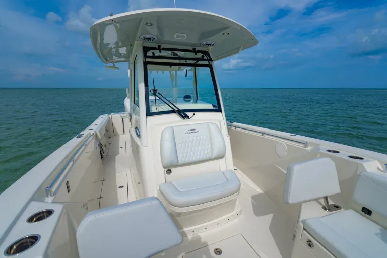 Cobia 320 CC forward console with Cobia-branded seat back, glass windshield with wiper, and bow lounge seating area visible