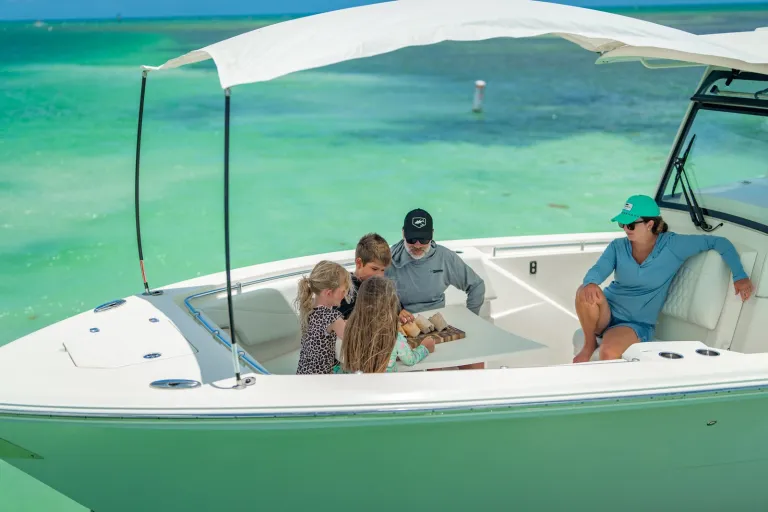 Cobia 320 CC anchored at sandbar with family gathered around bow table having lunch in shallow turquoise water
