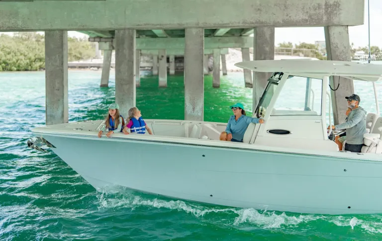 Cobia 320 CC family with kids at bow and adults at helm passing under Keys bridge over green water