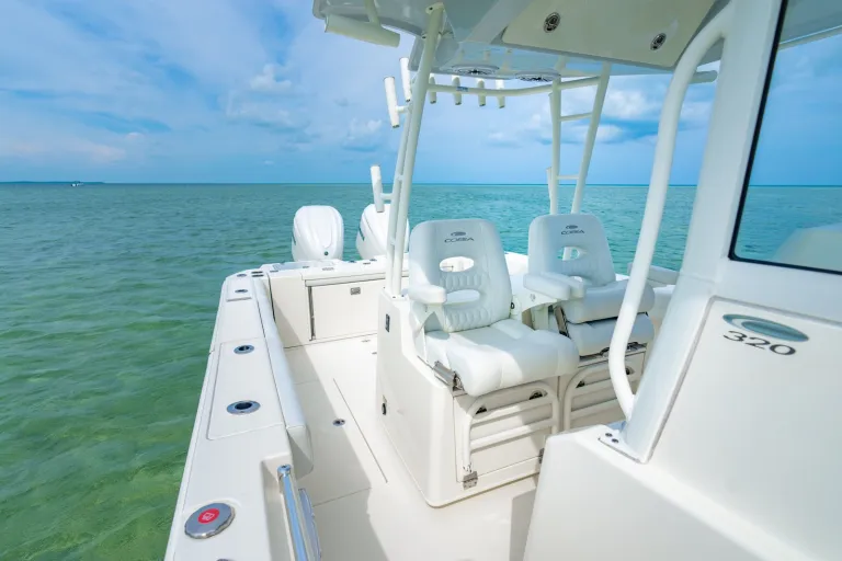 Cobia 320 CC dual white captain's chairs at helm station with hardtop, outriggers, and 320 model badge on center console