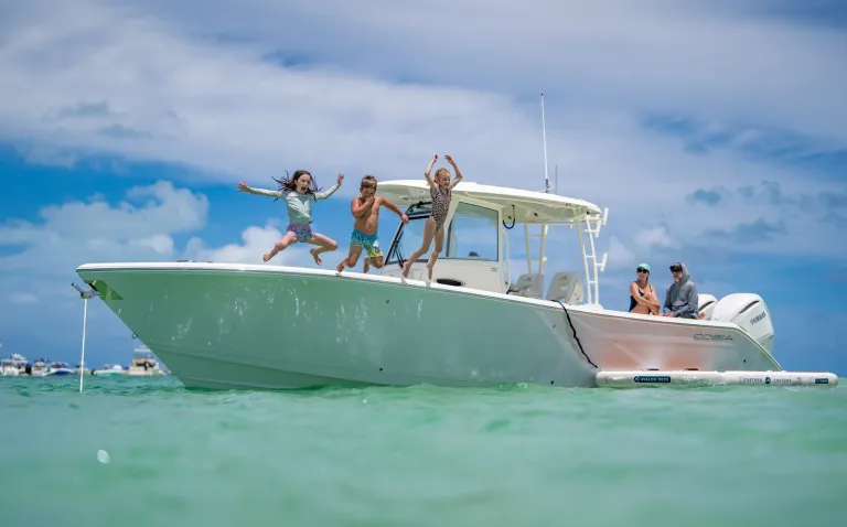 Three kids jumping off the bow of a Cobia 320 CC at a sandbar with parents watching over turquoise water