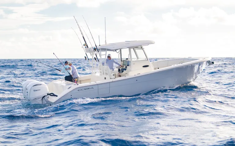 Cobia 320 CC port-quarter running shot with three anglers fishing over deep blue offshore water
