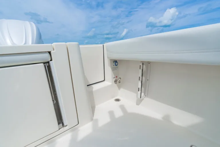 Cobia 320 CC inward-opening side boarding door open showing cockpit access, freshwater washdown faucet, and under-seat storage