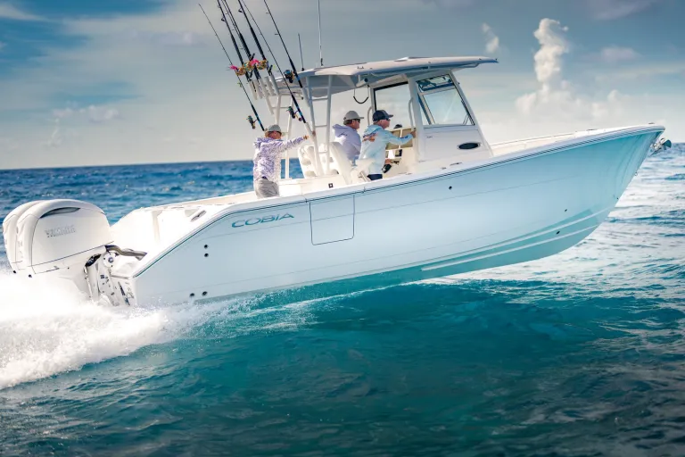 Cobia 320 CC starboard-bow angle with two anglers, prominent Cobia branding on hull, turquoise water