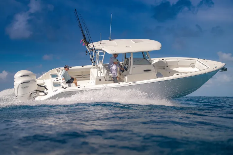 Starboard side profile of Cobia 320 CC with three anglers and twin Yamaha outboards running offshore