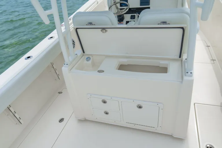Cobia 320 CC tackle station with open lid exposing tackle tray compartments and lower storage drawers with ocean in background