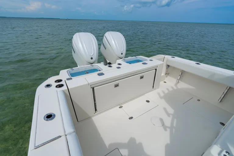 Cobia 320 CC stern view showing twin Yamaha outboard motors, two open livewells, transom storage cabinet, and calm water