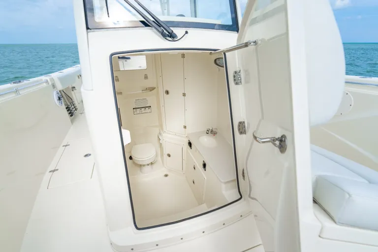 Cobia 320 CC forward-entry console door open showing spacious walk-down head with electric macerator toilet, sink, and storage closet