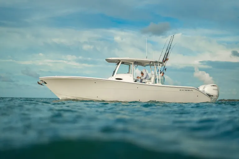 Water-level port side profile of white Cobia 320 CC with angler at helm, Yamaha outboard, cloudy sky