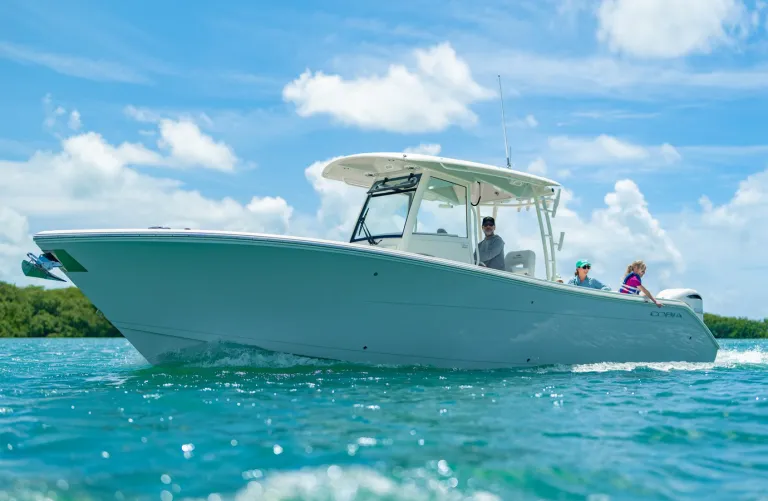 Three kids jumping off the bow of a Cobia 320 CC at a sandbar with parents watching over turquoise water