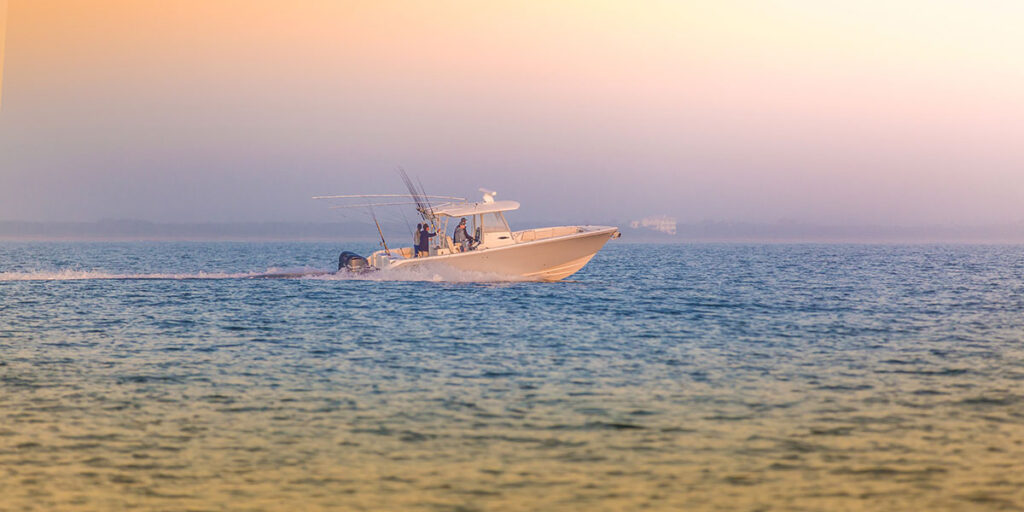Distant view of a Cobia 320 Center Console with orange and pink sky.